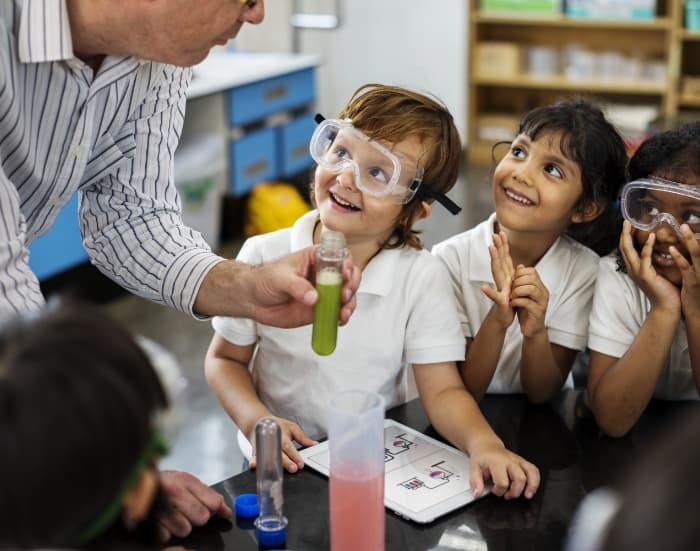 Crianças fazendo experimentos e encarando seu professor de química num laboratório